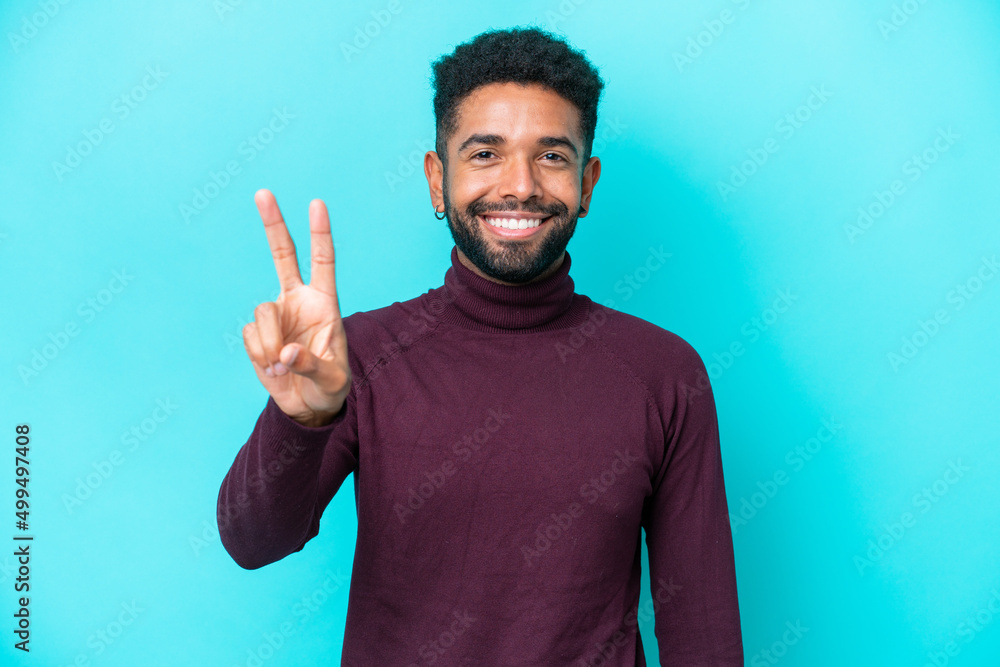 Fototapeta premium Young Brazilian man isolated on blue background smiling and showing victory sign
