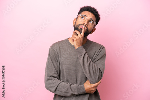 Young Brazilian man isolated on pink background having doubts while looking up