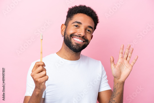 Young Brazilian man brushing teeth isolated on pink background saluting with hand with happy expression