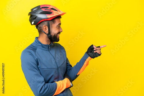 Young cyclist Brazilian man isolated on yellow background pointing finger to the side and presenting a product