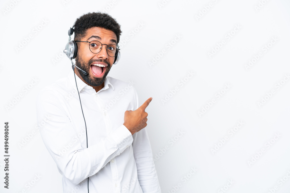 Telemarketer Brazilian man working with a headset isolated on white background surprised and pointing side Telemarketer Brazilian man working with a headset isolated on white background surprised and pointing side