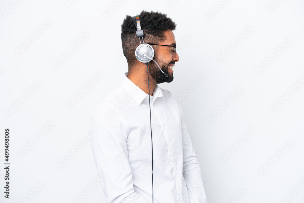 Telemarketer Brazilian man working with a headset isolated on white background laughing in lateral position