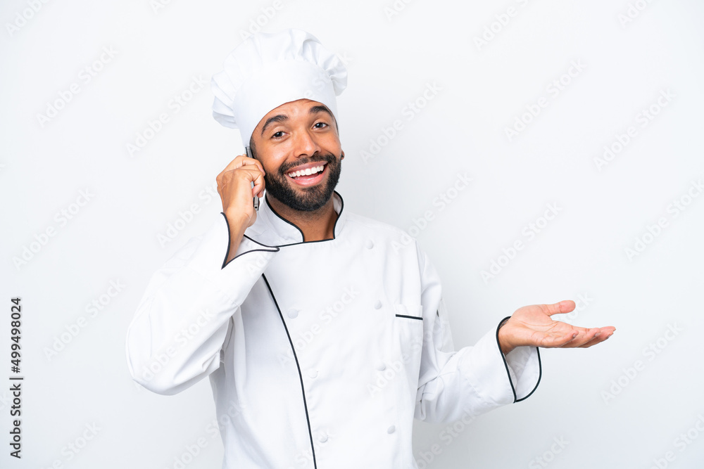 Young Brazilian chef man isolated on white background keeping a conversation with the mobile phone with someone Young Brazilian chef man isolated on white background keeping a conversation with the mobile phone with someone