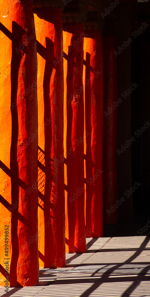 Fototapeta premium abstract design of of black shadows on vibrant orange wooden pillars shadows of fence cast on pillars in afternoon sunlight in down town Santa Fe New Mexico near plaza colorful vertical backdrop 