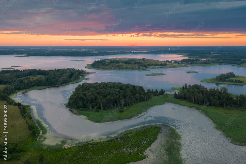 Amazing lake land from above, beautiful islands covered with trees and meadows in morning sunlight. Aerial, flight over lakes during fantastic sunrise. Colorful clouds in sky on horizon