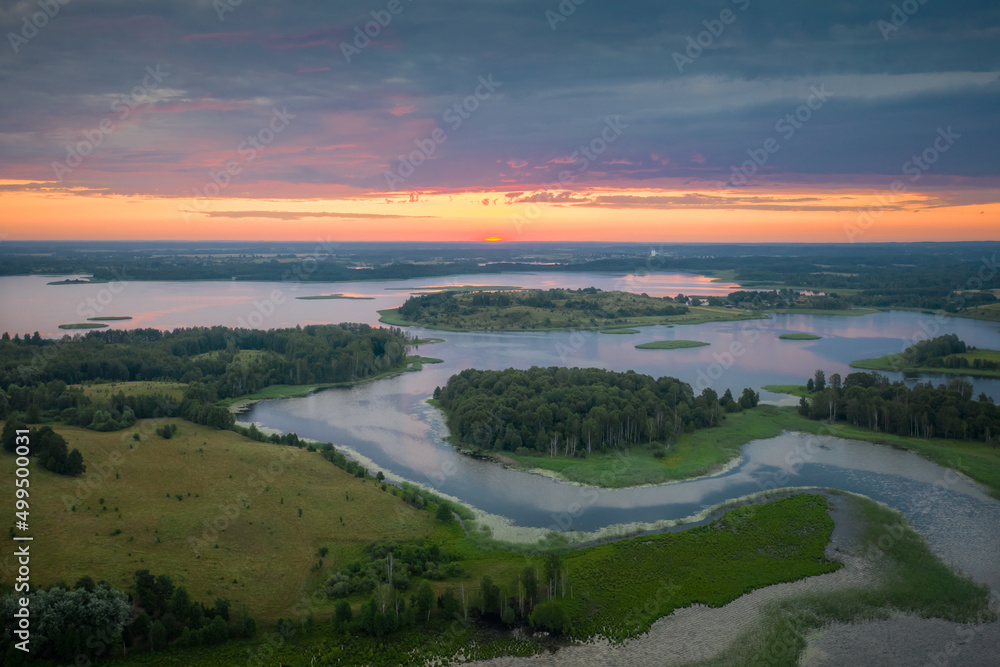 Amazing lake land from above, beautiful islands covered with trees and meadows in morning sunlight. Aerial, flight over lakes during fantastic sunrise. Colorful clouds in sky on horizon