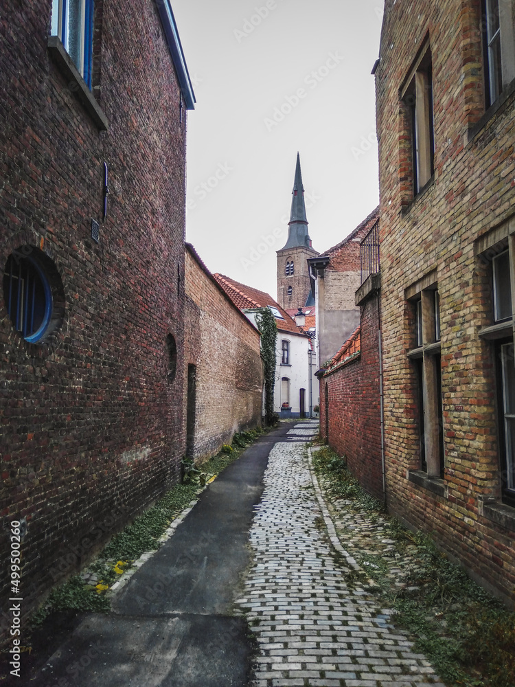 A narrow historical street with medieval brick houses and a tower of a church, Bruges town, Belgium
