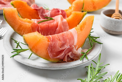 Italian antipasti. Melon cantaloupe slices with prosciutto ham, rosemary and honey in a plate on white background
