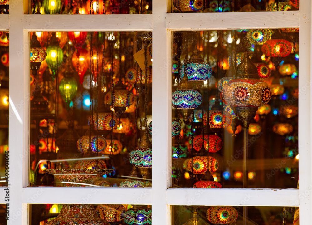 Fototapeta premium traditional style colored glass lanterns and lights hanging in shop window shot through glass window with white window frame visible detailed painted glass lanterns as souvenirs or interior home 