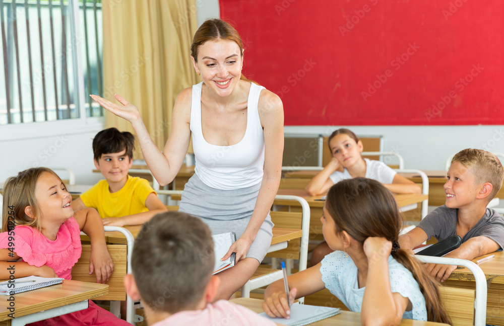 Fototapeta premium Friendly young female teacher working with preteen pupils in classroom at elementary school..