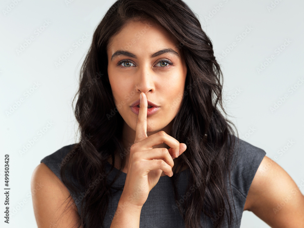 Everyone wants in on the secret. Shot of a beautiful young woman posing with her finger on her lips. Everyone wants in on the secret. Shot of a beautiful young woman posing with her finger on her lips.
