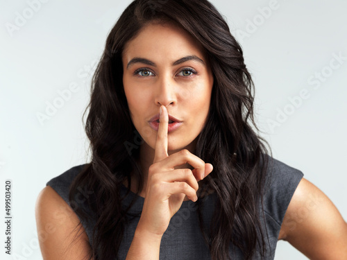 Everyone wants in on the secret. Shot of a beautiful young woman posing with her finger on her lips.