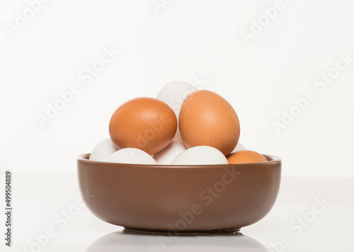 brown bowl with white and brown chicken eggs on white background