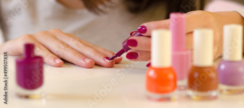 Young woman painting nails during manicure using purple nail varnish at home
