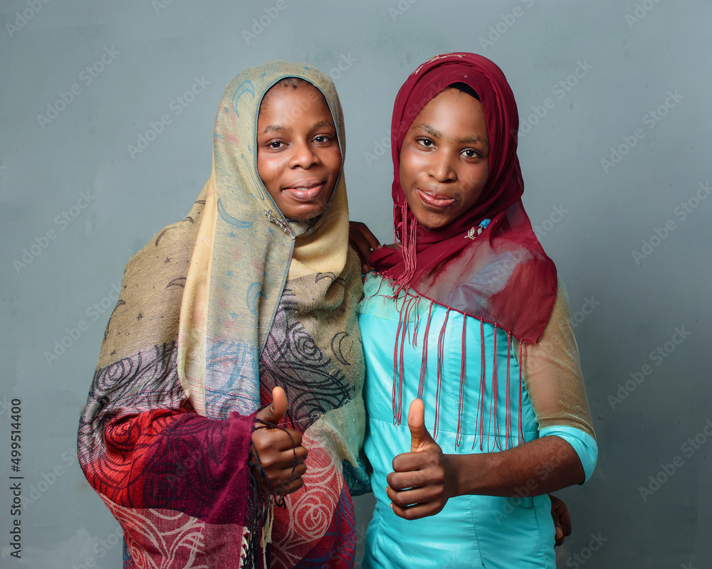 Two happy African Nigerian female muslim sisters or friends with Hijab  scarf, prepared to engage the