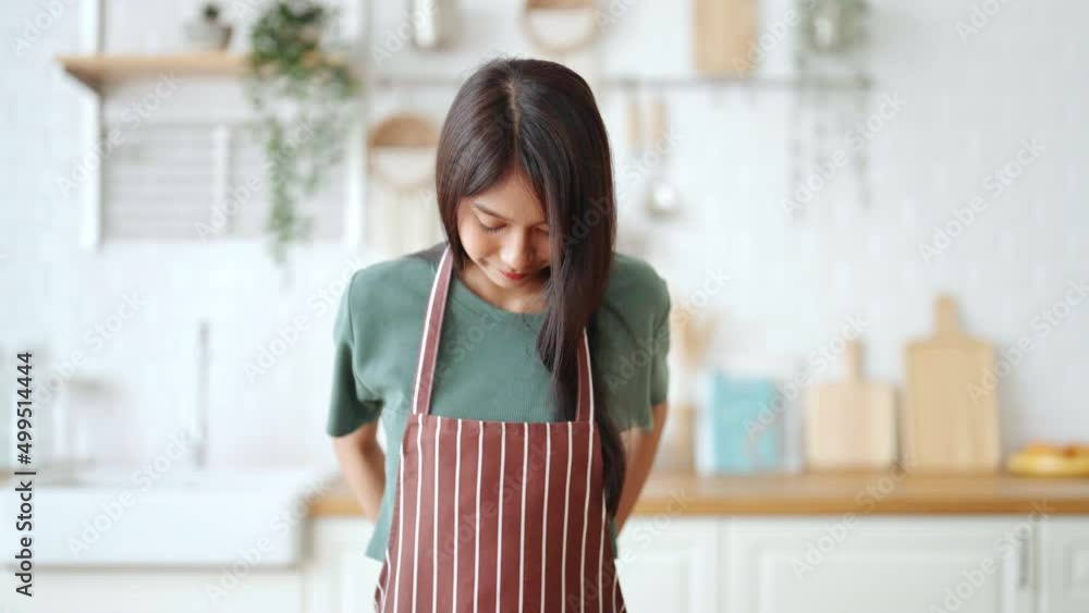 Happy young asian woman wearing apron and standing in kitchen room. Beautiful female smiling and looking at camera feeling confident Happy young asian woman wearing apron and standing in kitchen room. Beautiful female smiling and looking at camera feeling confident