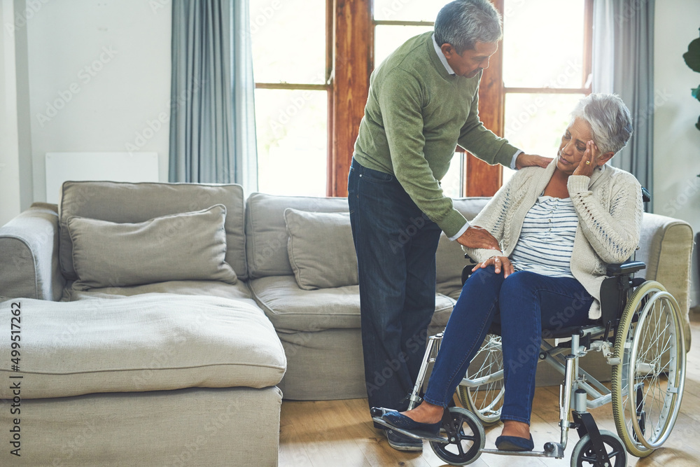 We will get through this together. Shot of a worried looking elderly woman seated in a wheelchair while being supported and held by her husband inside at home during the day. We will get through this together. Shot of a worried looking elderly woman seated in a wheelchair while being supported and held by her husband inside at home during the day.