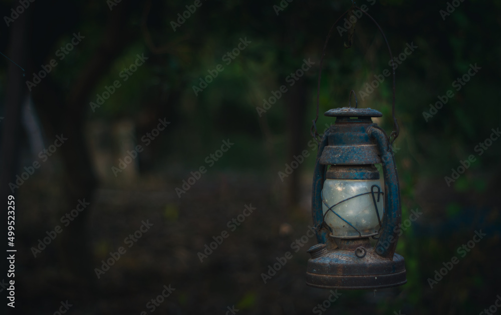 Rusty old lantern hangs in the forest, vintage lamp in dark tone