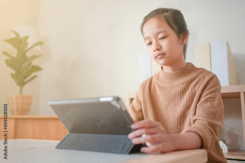 Asian kid studying online using tablet in a living room alone. Asian kid studying online using tablet in a living room alone.