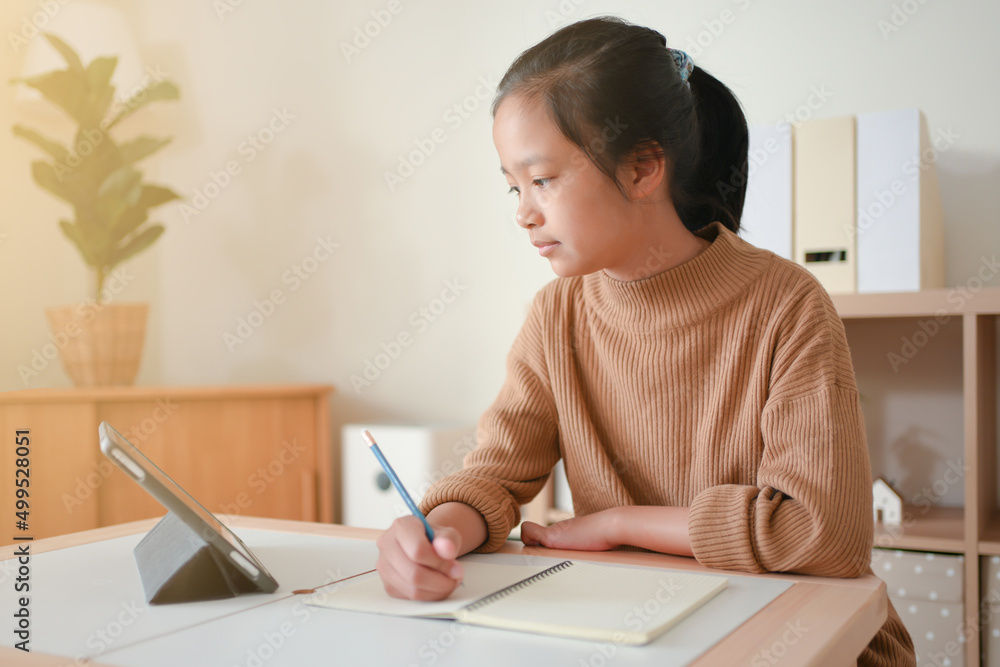 Asian kid studying online using tablet in a living room alone. Asian kid studying online using tablet in a living room alone.