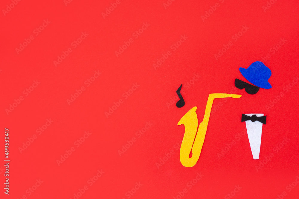 Jazz Day. Silhouette of a musician with a saxophone from which melodies flew out, on a red background, cutted out of felt. Flat lay. Copy space