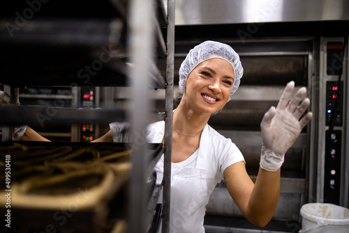 Photos Portrait of female baker in white clean uniform and hairnet moving trays with bread in bakery production