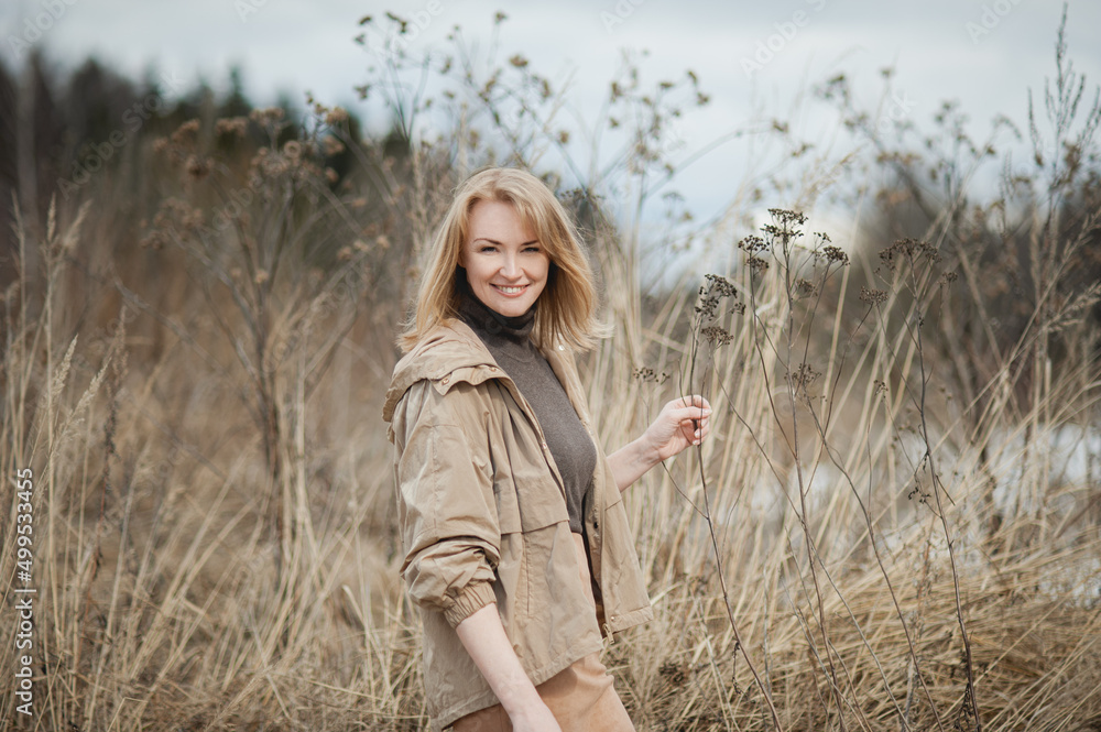 A portrait of a laughing, attractive middle-aged blonde woman in a beige jacket in early spring. A portrait of a laughing, attractive middle-aged blonde woman in a beige jacket in early spring.