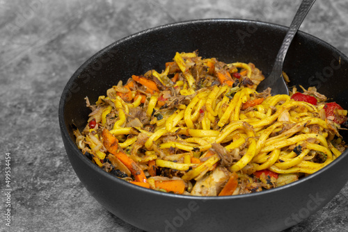 Shredded duck stir fry with spices and vegetables in a black bowl. On a stone background