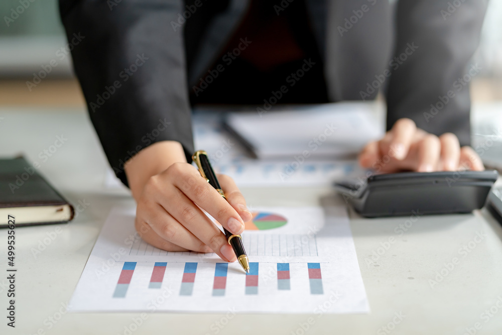 Business woman hand pointing to a financial data graph and presses the calculator to calculate the income budget.