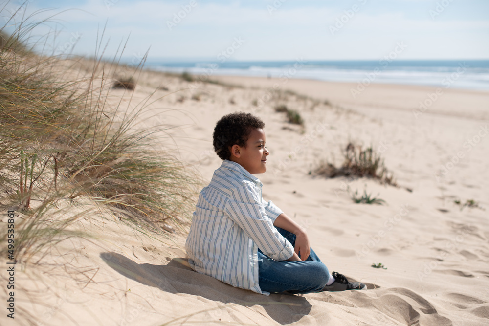 Back view of beautiful African American boy. Male model with curly hair in casual clothes sitting on sand. Portrait, beauty concept Back view of beautiful African American boy. Male model with curly hair in casual clothes sitting on sand. Portrait, beauty concept
