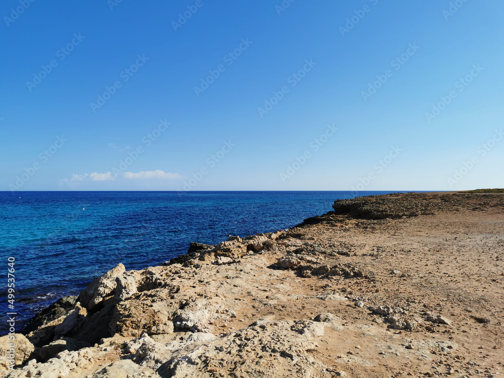View from the rocky shore to the blue sea to the horizon against a blue sky with clouds. View from the rocky shore to the blue sea to the horizon against a blue sky with clouds.