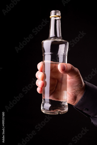 Bottle with alcohol in hand on a black background.