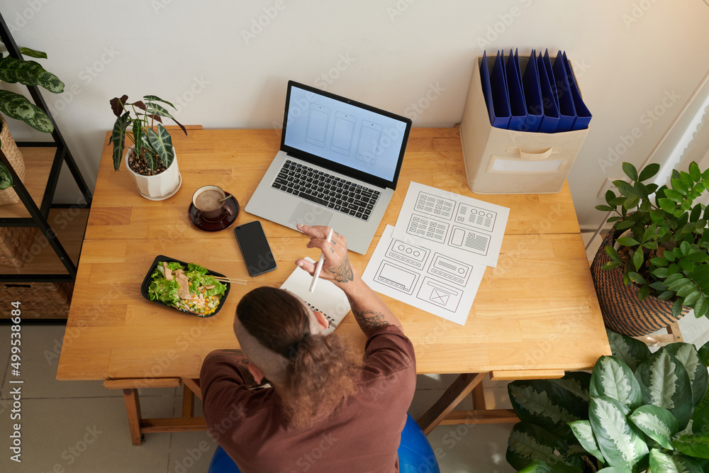 UI designr eating lunch at desk in his home office when working on wireframe of interface design UI designr eating lunch at desk in his home office when working on wireframe of interface design