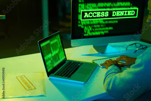 Your secret files arent safe from me. Shot of an unrecognizable hacker cracking a computer code in the dark. photo