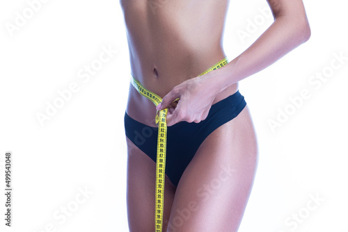 Closeup of Good Fit Sexy Slim Caucasian Woman Body taking Measure Reading With Tape Measure in Hand In Front of Black Thong Isolated on White Background