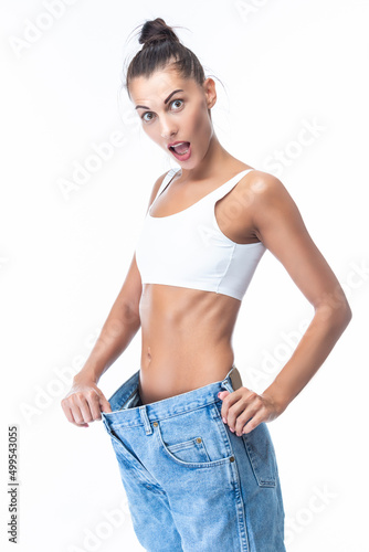 Surprised Positive Good Fit Sexy Slim Caucasian Woman Posing in Lose Oversized Jeans Demonstrting Dieting and Weight Lose Concepts Isolated Over White Background.
