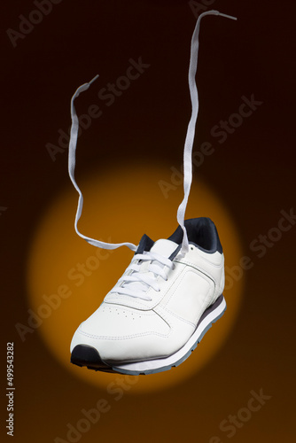 Levitating Shoes Concepts. Pair of New White Sneakers With Flying Shoelaces Placed Over Yellow Background With Circular Spotlight.