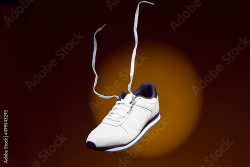 Levitating Shoes Concepts. Pair of New White Sneakers With Flying Shoelaces Placed Over Yellow Background With Circular Spotlight