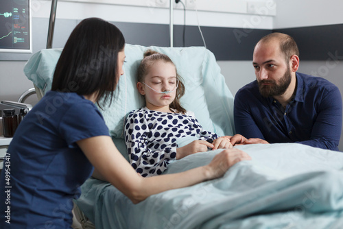 Restless uneasy careful parents conversating about little girl illness evolution while in pediatric hospital patient recovery ward room. Worried nervous young people talking about healthcare treatment