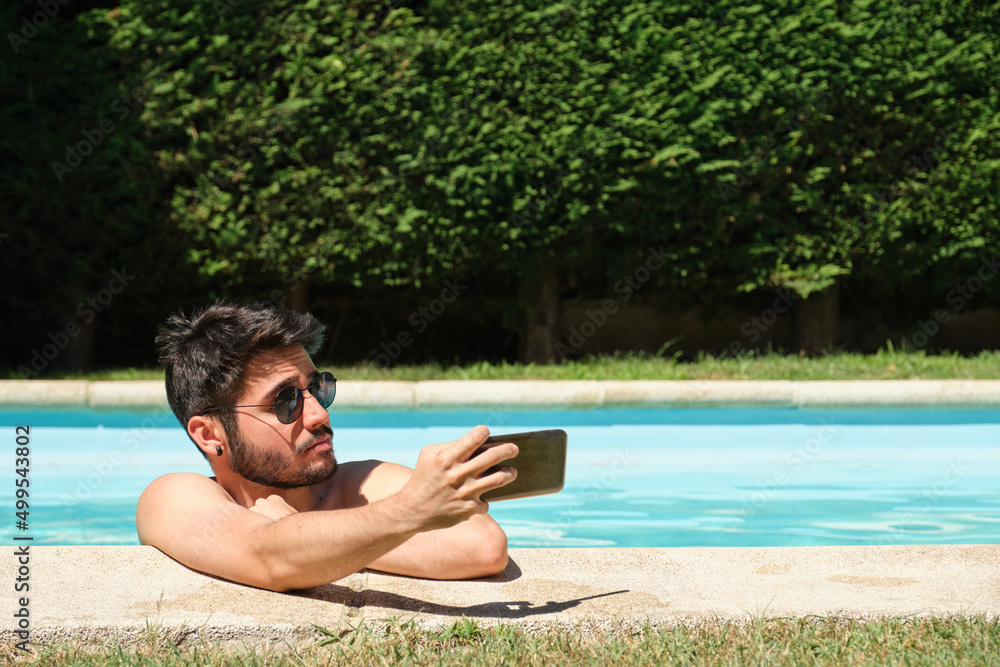 Young man wearing sunglasses, taking a selfie in a swimming pool.