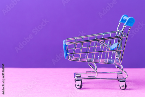 One Empty Trolley Shopping or Sale Cart Placed Over Seamless Solid Purple Violet Background With Copy Space.