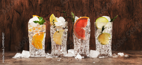 Gin tonic and citrus cocktails set. Summer drinks with lime, lemon, grapefruit, orange, soda and herbs in highball glasses, wooden counter background, cocktail party