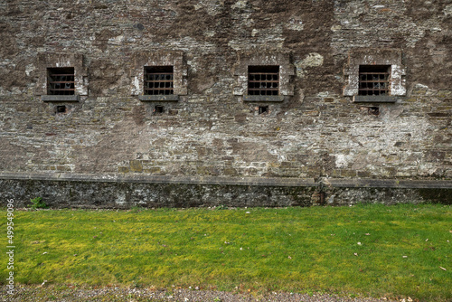 Small windows with metal bars in a jail. Hard conditions. History of criminal correction system. Weathered stone wall. Cork Gaol, Ireland. Male and female prison.