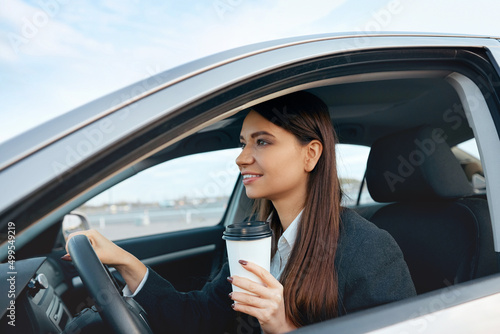 Happy young woman with coffee to go driving her car