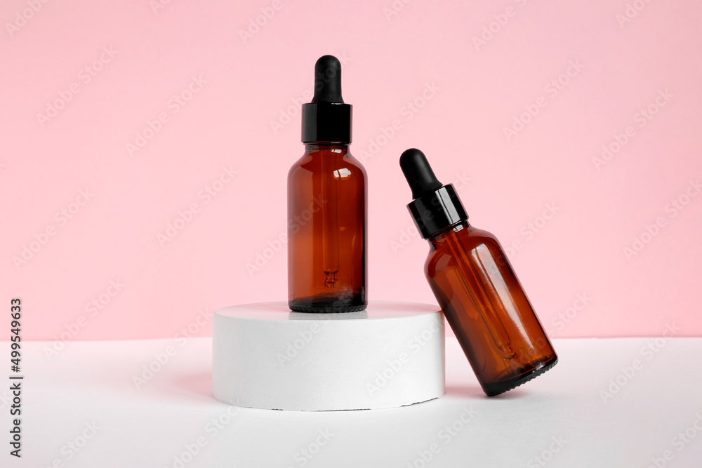 Amber glass dropper cosmetic bottles, white podium. Natural skin care SPA beauty product design. Mineral organic oil on pink background. Mock-Up. Oily pipette. Face and body treatment. Front view Amber glass dropper cosmetic bottles, white podium. Natural skin care SPA beauty product design. Mineral organic oil on pink background. Mock-Up. Oily pipette. Face and body treatment. Front view