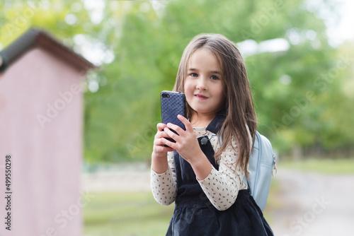 happy and healthy childhood. little girl with backpack using smartphone outside. the child is coming from school