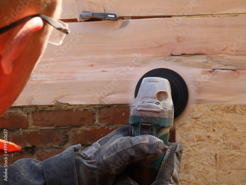 the movement of a round emery nozzle on a grinder in the hands of a man in glasses visible from the back in the process of smoothing the surface of a wooden texture board photo