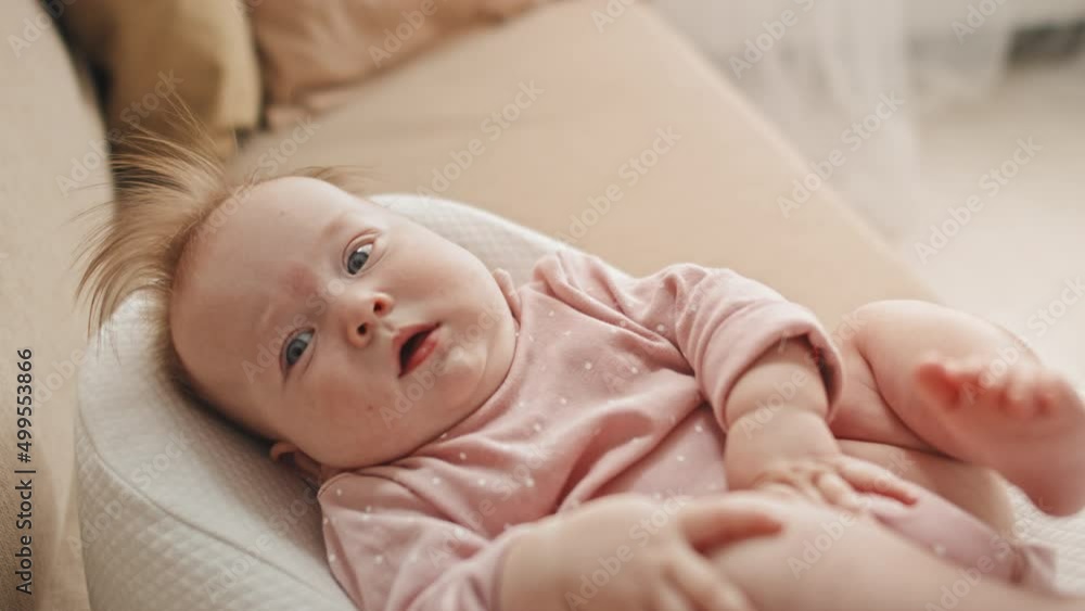 Medium long of adorable blue-eyed Biracial infant in pink onesie with pacifier lying in baby nest on couch at home Medium long of adorable blue-eyed Biracial infant in pink onesie with pacifier lying in baby nest on couch at home