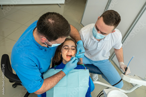 Dentist and assistant in mask treats teeth female patient at the dental office