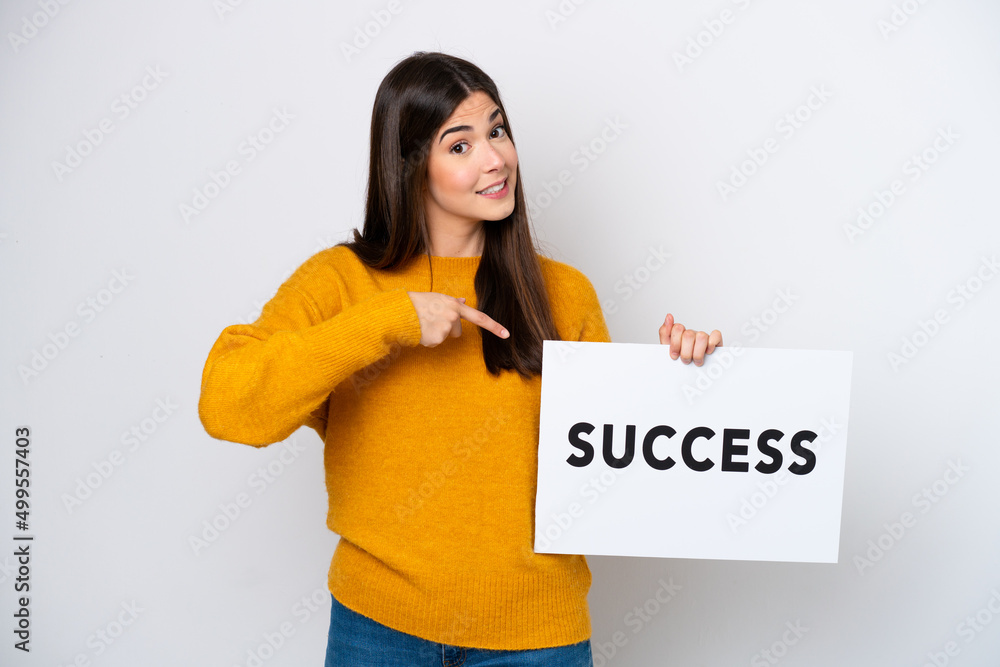 Young Brazilian woman isolated on white background holding a placard with text SUCCESS and pointing it Young Brazilian woman isolated on white background holding a placard with text SUCCESS and pointing it